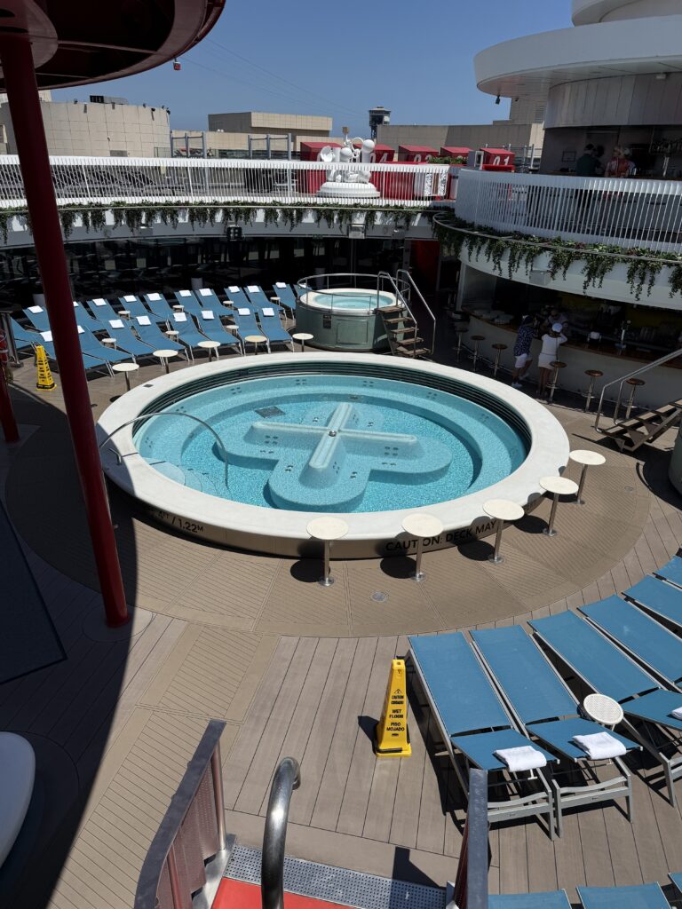 Circular hot tub on the Virgin Voyages Aquatic Club pool deck surrounded by loungers, relaxation areas and modern cruise ship design.