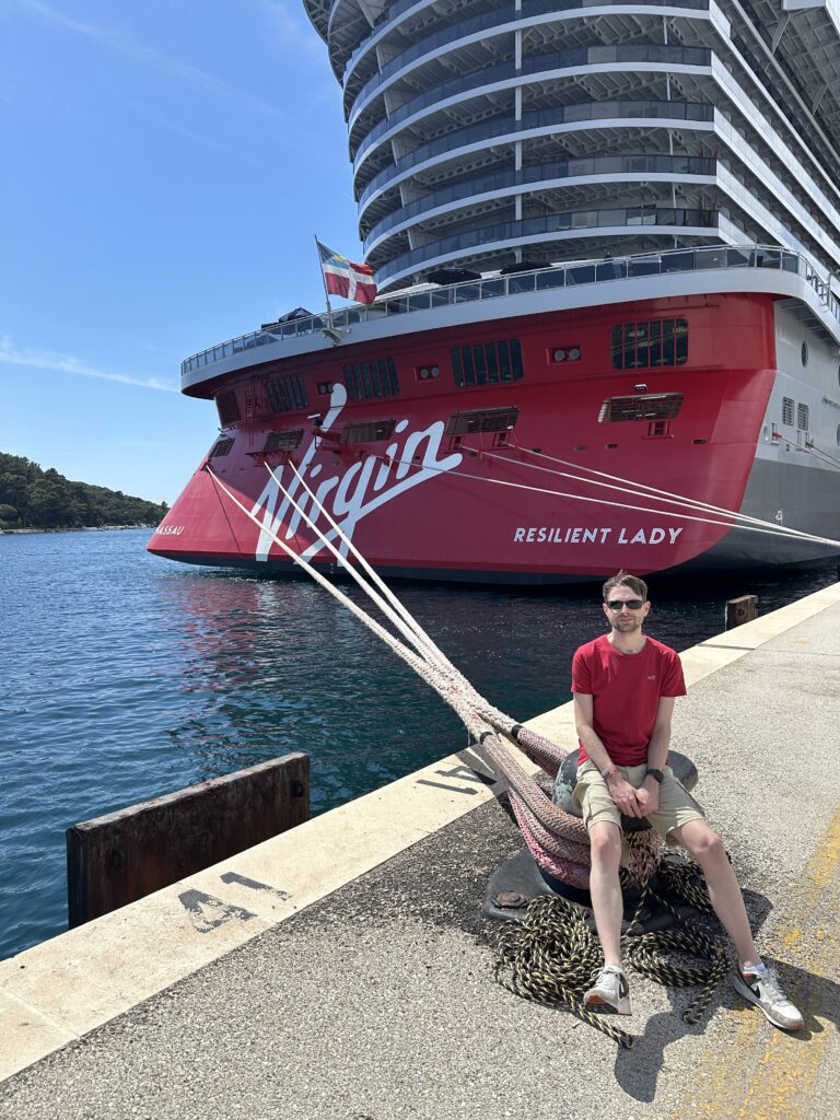 Resilient Lady by Virgin Voyages docked in port with the iconic red hull and Virgin branding visible, captured during a cruise ship visit by an Award Winning Gold Virgin Voyages First Mate.