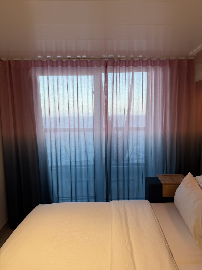 Virgin Voyages Sea Terrace cabin featuring a comfortable bed, floor-to-ceiling balcony doors and ocean views from a private terrace.