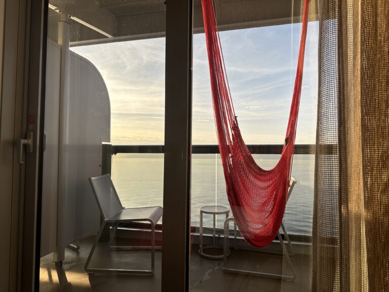 Virgin Voyages Sea Terrace cabin balcony featuring the iconic red hammock overlooking calm ocean views at sunrise.