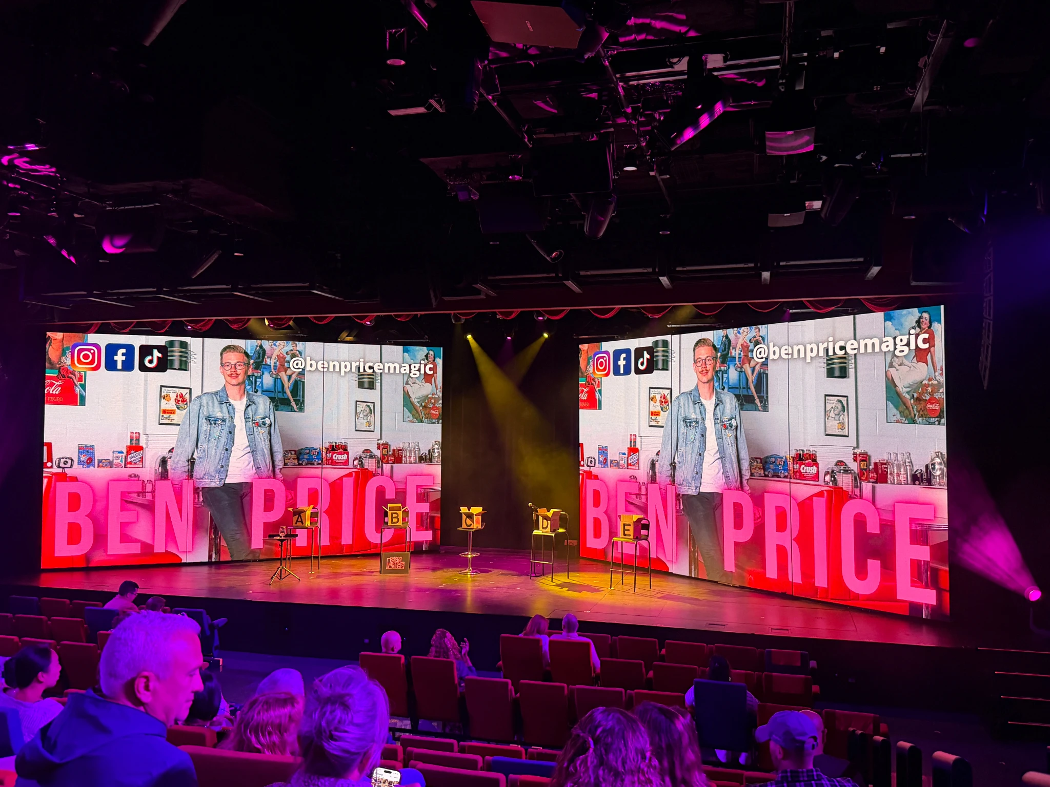 Ben Price Magic performing as a guest entertainer onboard Virgin Voyages in The Red Room theatre, with large digital screens, stage lighting and seated audience members.