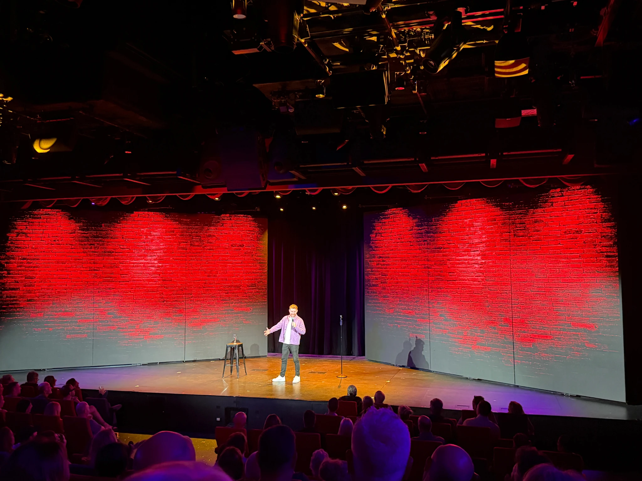 Comedian Gareth Waugh performing live on the Festival Stage aboard a Virgin Voyages cruise ship, entertaining guests during an evening show.