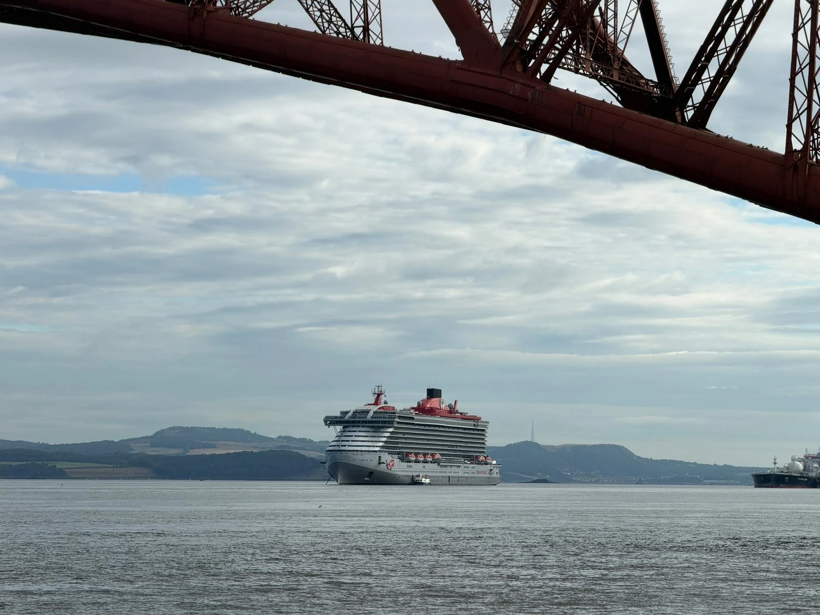 Virgin Voyages cruise ship anchored in the Firth of Forth near Hawes Pier, Edinburgh, viewed beneath the iconic Forth Bridge in Scotland.