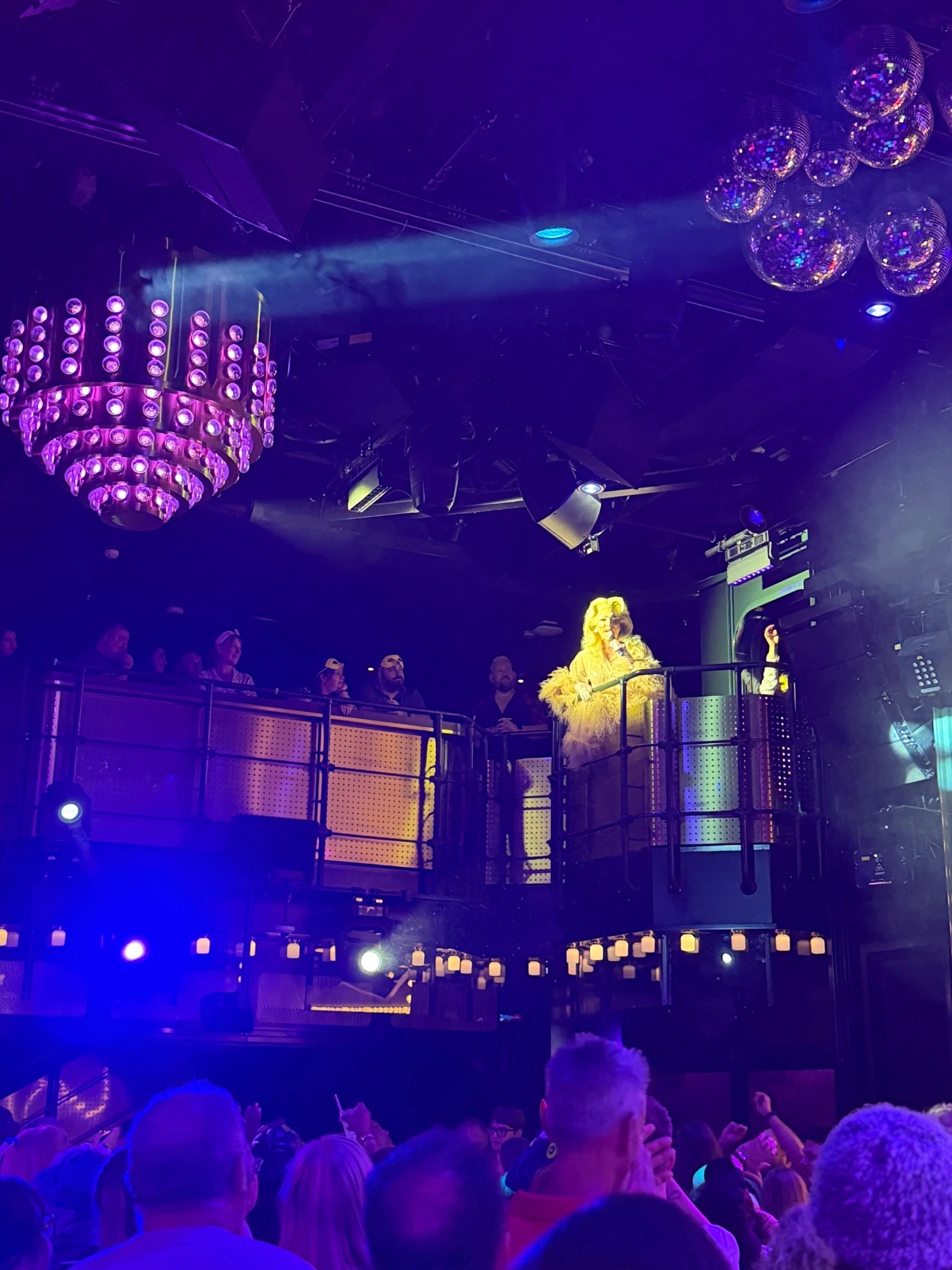 Guests enjoying the Virgin Voyages PJ Party inside The Manor nightclub, with purple lighting, disco balls and live entertainment overlooking the dance floor with The Diva.